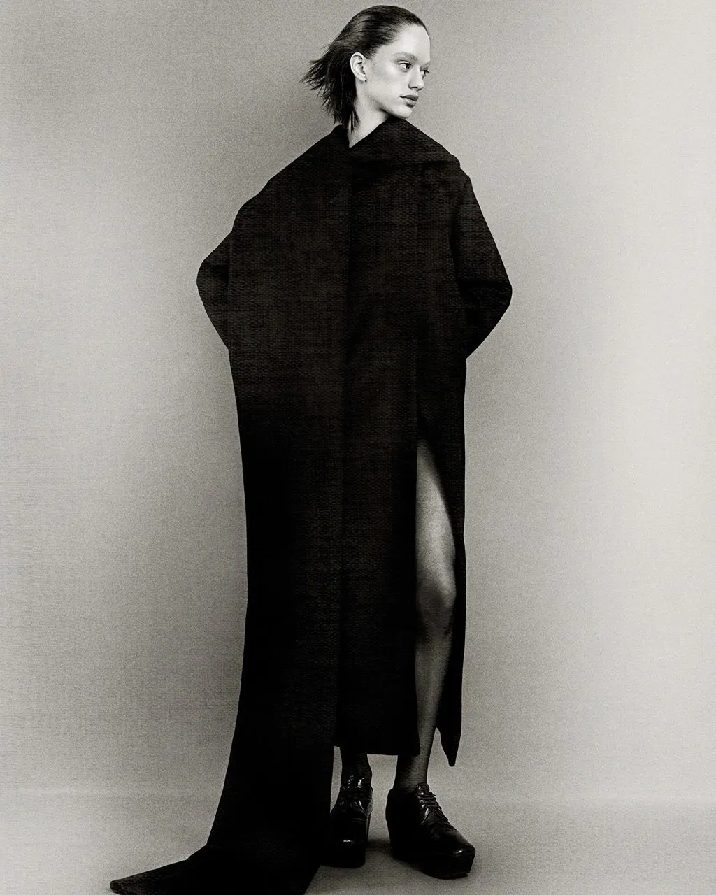 Full-length black coat with an oversized collar, shot in studio against pale grey