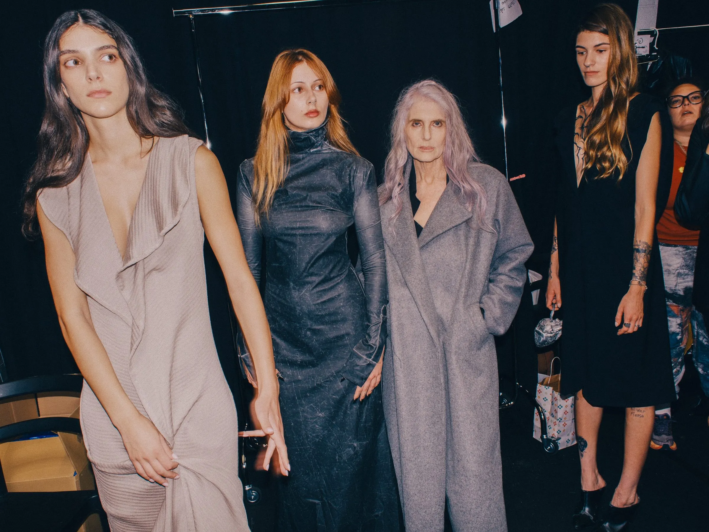 Group of models backstage in the collection: pale draped coats alongside black tailoring