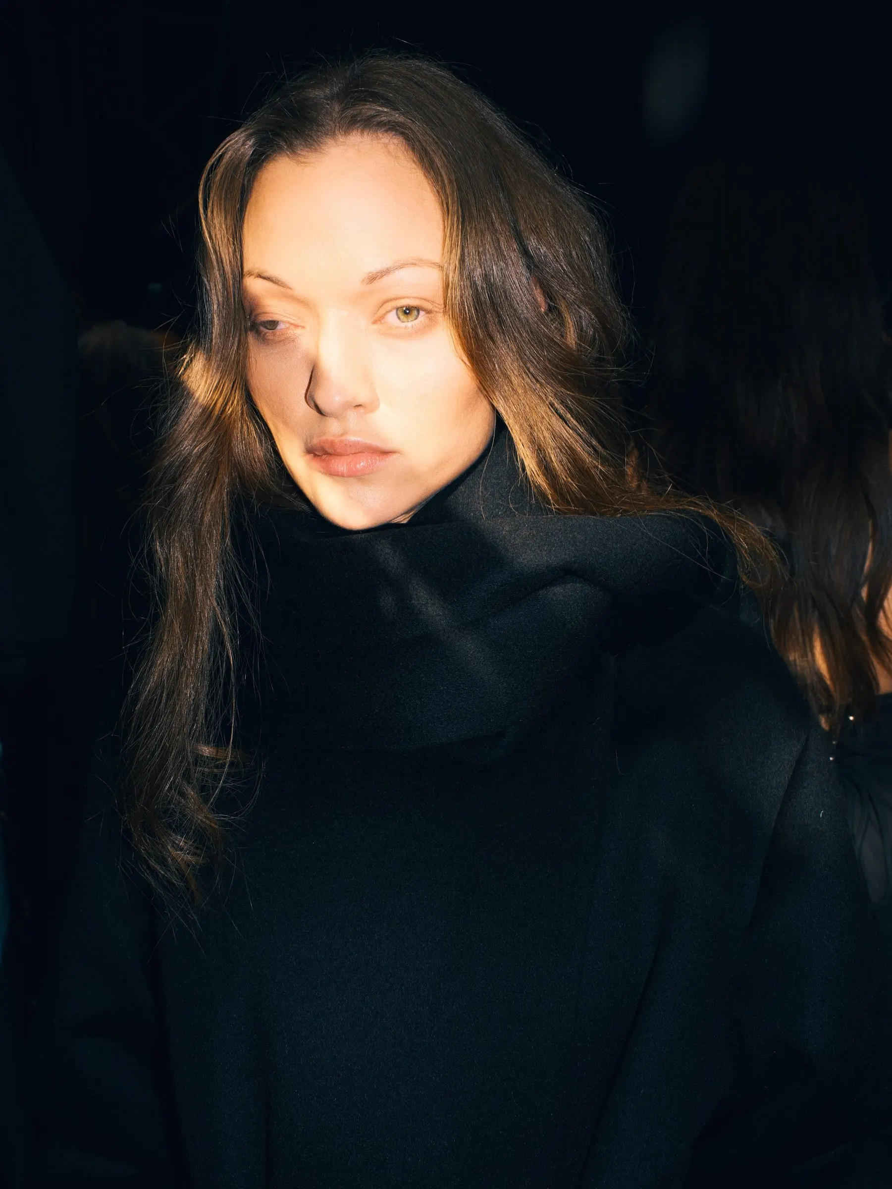 Close portrait in a black high-collared wool coat against a dark background