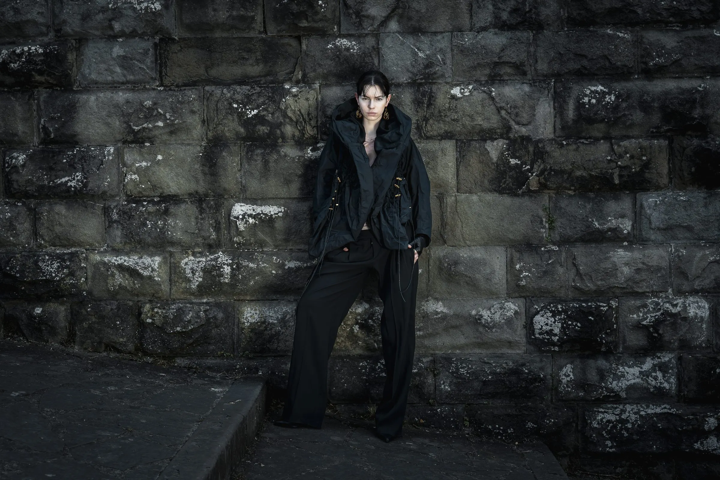 Full-length black tailored look photographed against a weathered stone wall at night