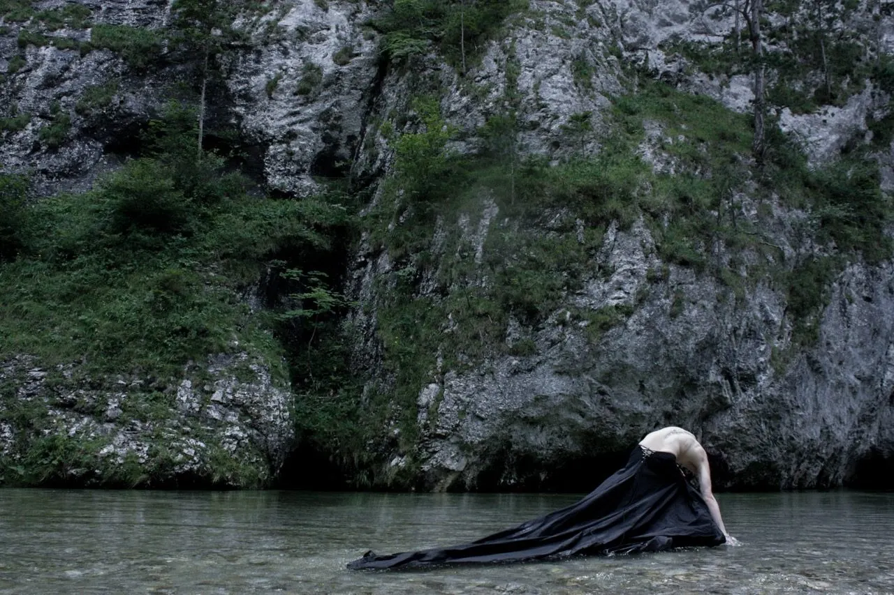 Black draped garment trailing into shallow water below a limestone gorge